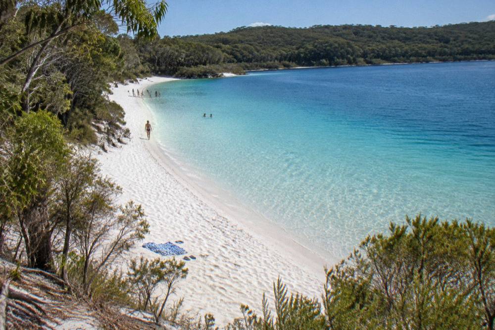 Clear freshwater lake with white sand shore surrounded by green forest