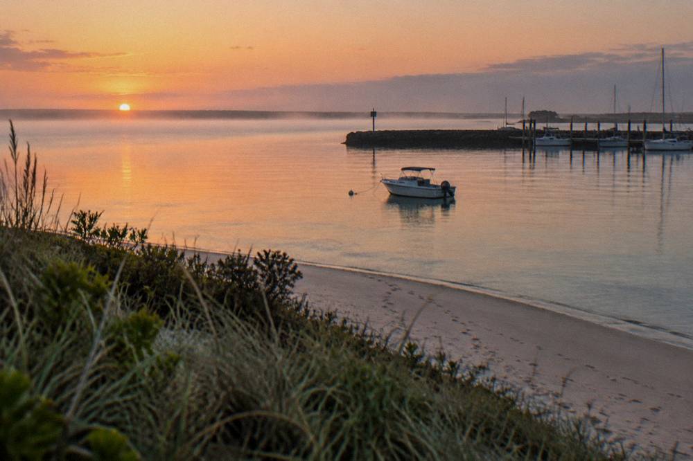 A calm bay at sunrise with a small boat at anchor near a sandy point