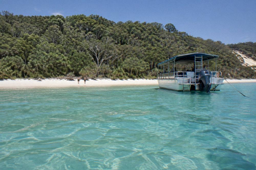 Small boat anchored beside a remote sandy beach with clear shallow water